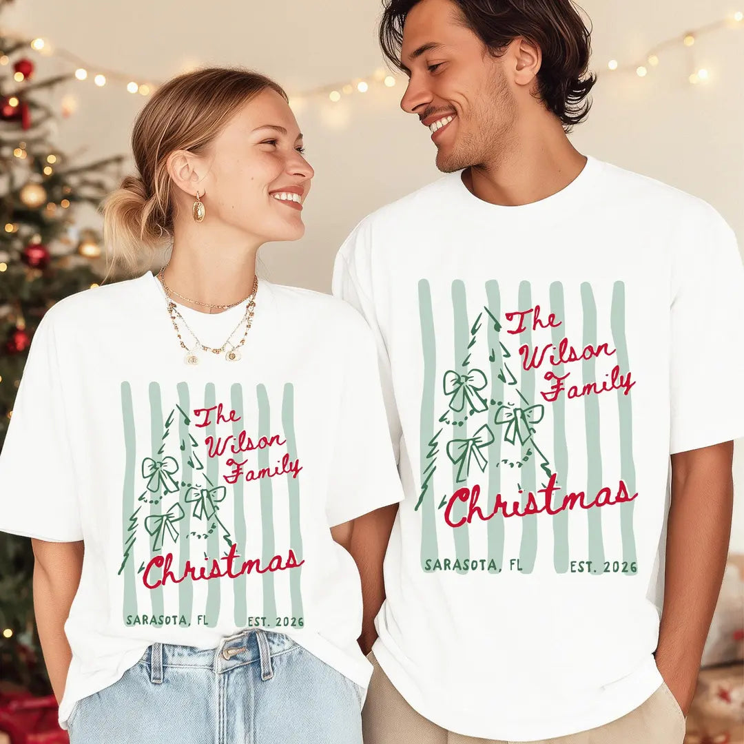 Woman and man by a christmas tree in White Comfort Colors tees, red The Wilson Family Christmas over a bow tree and stripes