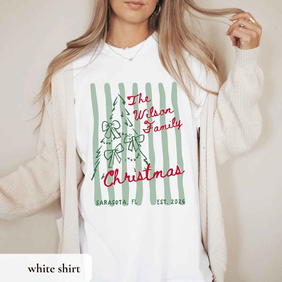 Woman in a White Comfort Colors tee and cream cardigan, red The Wilson Family Christmas with a bow tree on green stripes