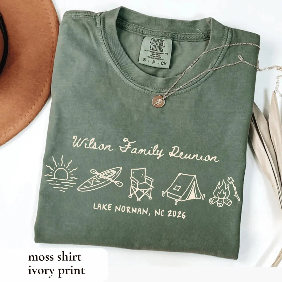 Folded Moss green Comfort Colors tee with ivory Wilson Family Reunion script, a row of camping icons and necklace on collar