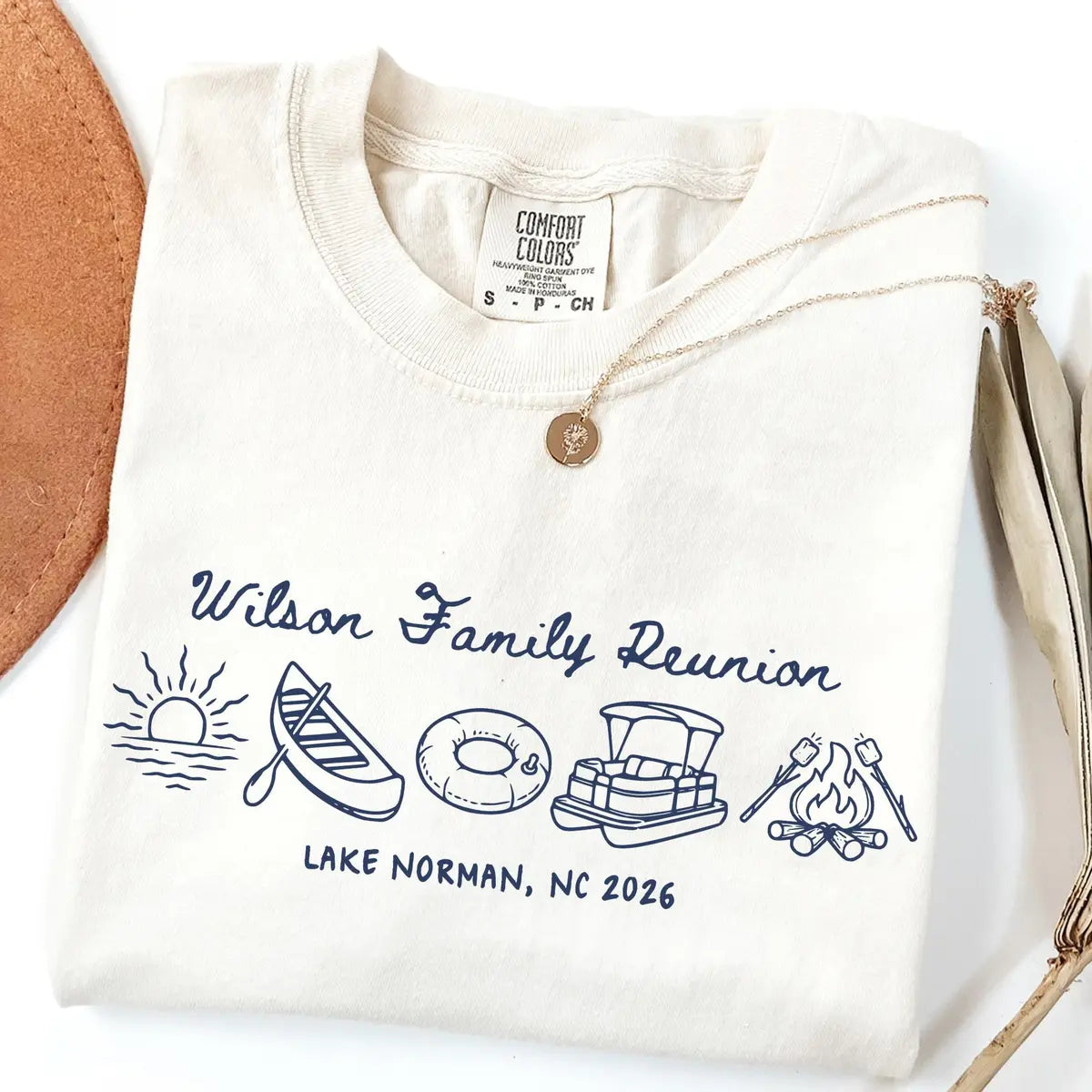 Folded Ivory Comfort Colors tee with navy Wilson Family Reunion script, sunrise, canoe, tube, pontoon boat and campfire