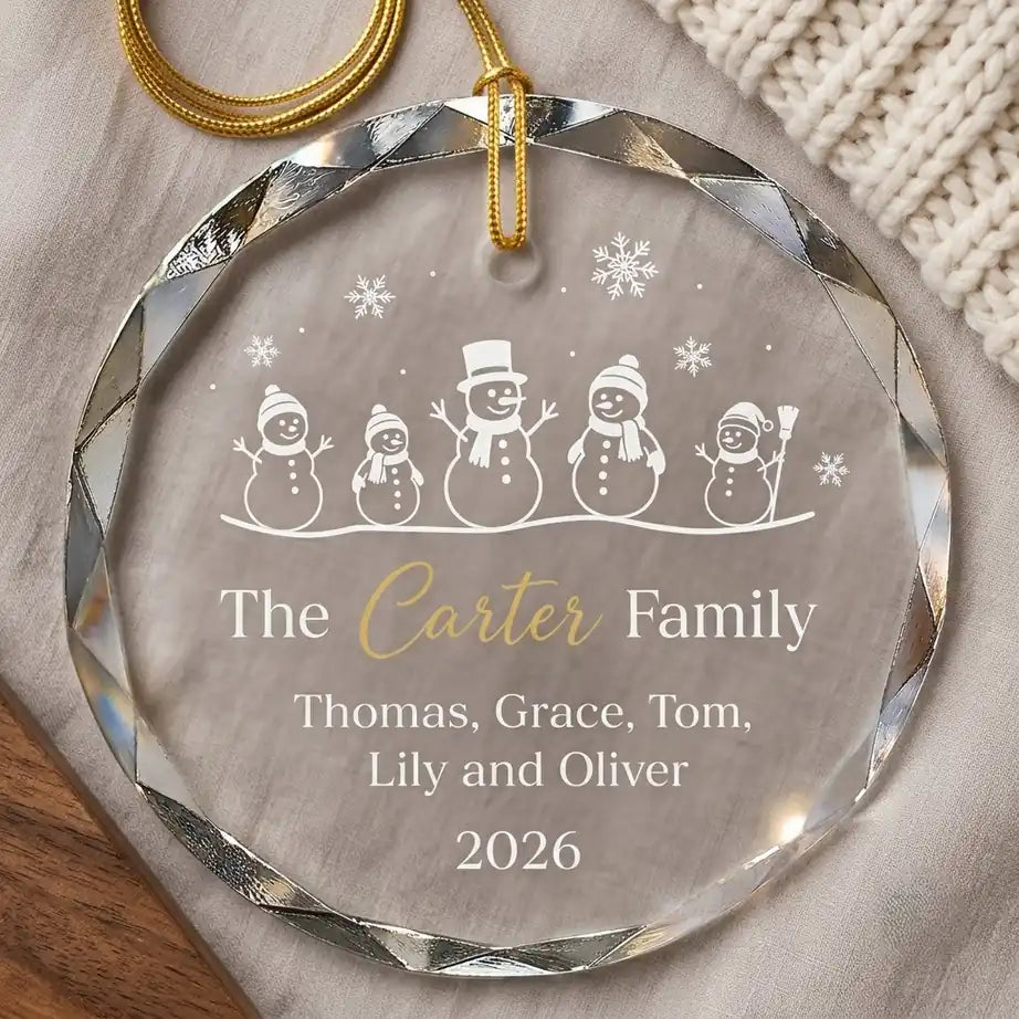 Clear glass round ornament laid flat on festive wooden surface with pine branches, pinecones and holiday decorations surrounding the family christmas design