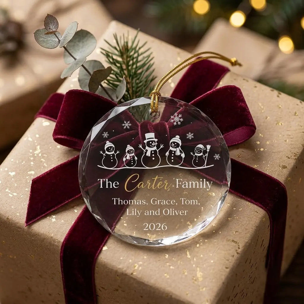 Personalized family christmas glass ornament presented beside a wrapped holiday gift box on rustic wooden background