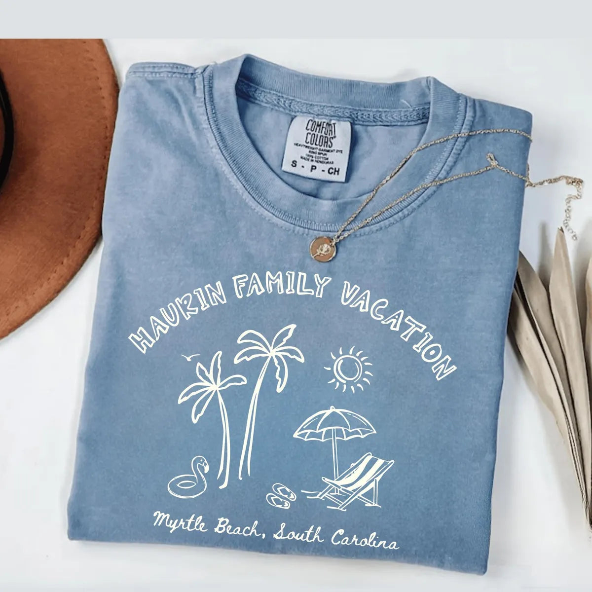 Folded Blue Jean Comfort Colors tee with white arched family vacation lettering, palms, sun, umbrella and Myrtle Beach