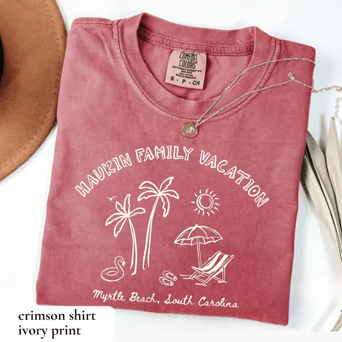 Folded Crimson Comfort Colors tee with ivory arched family vacation lettering, palms, sun, lounge chair and Myrtle Beach