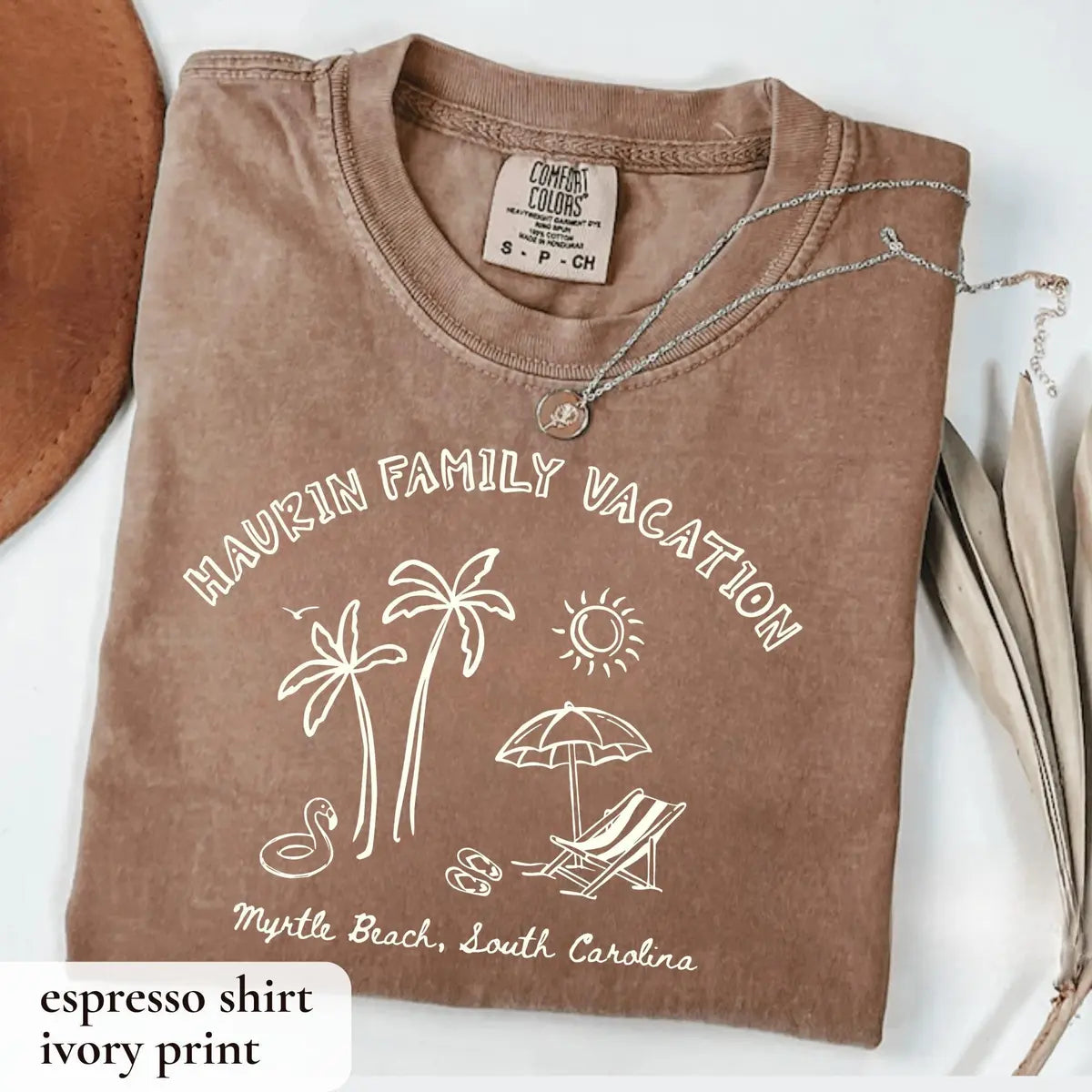 Folded Espresso brown Comfort Colors tee with ivory arched family vacation, palms, umbrella, lounge chair and flip flops
