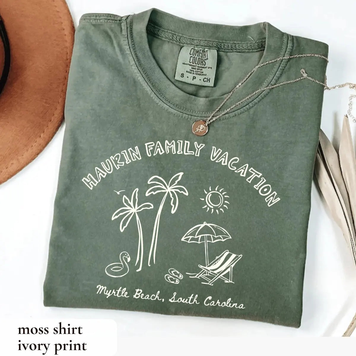 Folded Moss green Comfort Colors tee with ivory arched family vacation, palm trees, sun, umbrella and a flamingo float