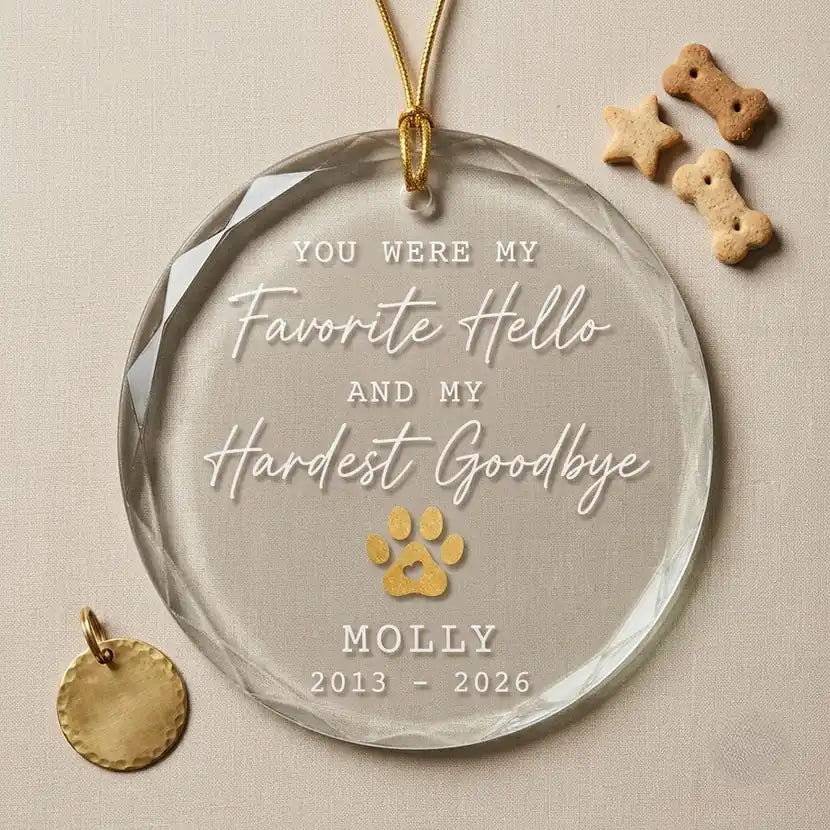 Clear glass round ornament laid flat on festive wooden surface with pine branches, pinecones and holiday decorations surrounding the pet memorial design