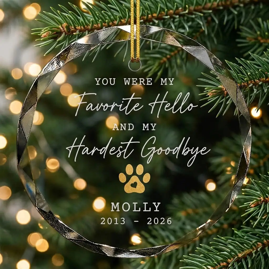 Personalized clear glass pet memorial ornament displayed hanging on Christmas tree branch with warm sparkling holiday lights background