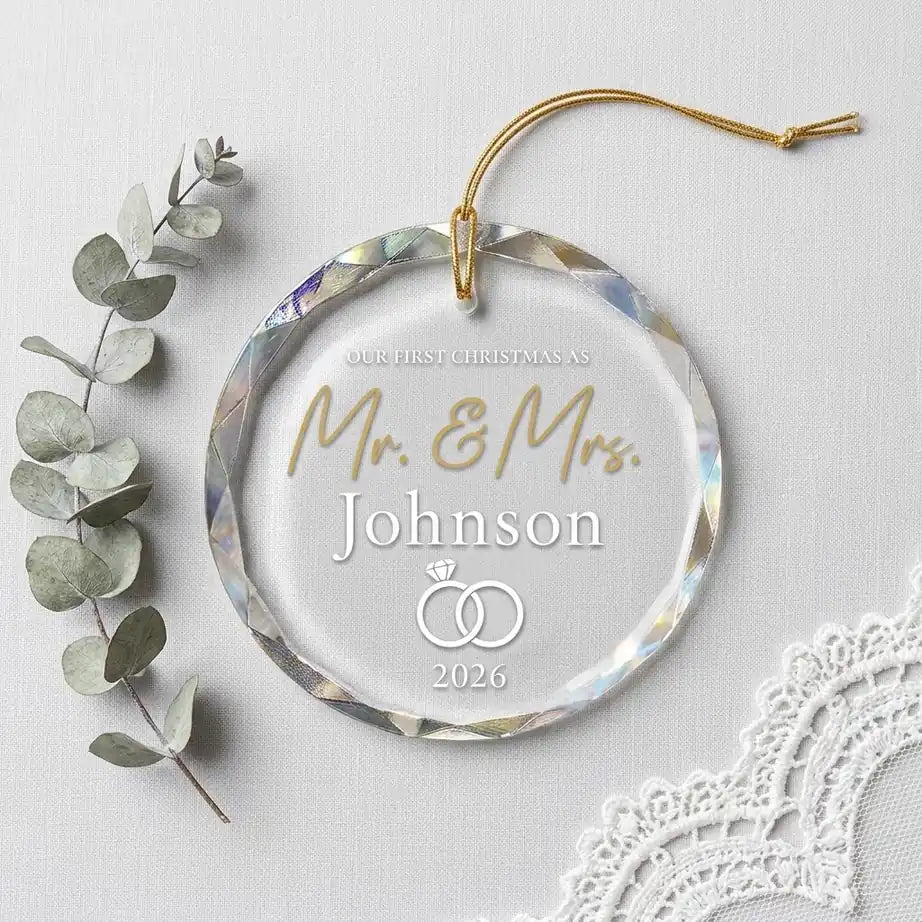Clear glass round ornament laid flat on festive wooden surface with pine branches, pinecones and holiday decorations surrounding the newlyweds wedding design