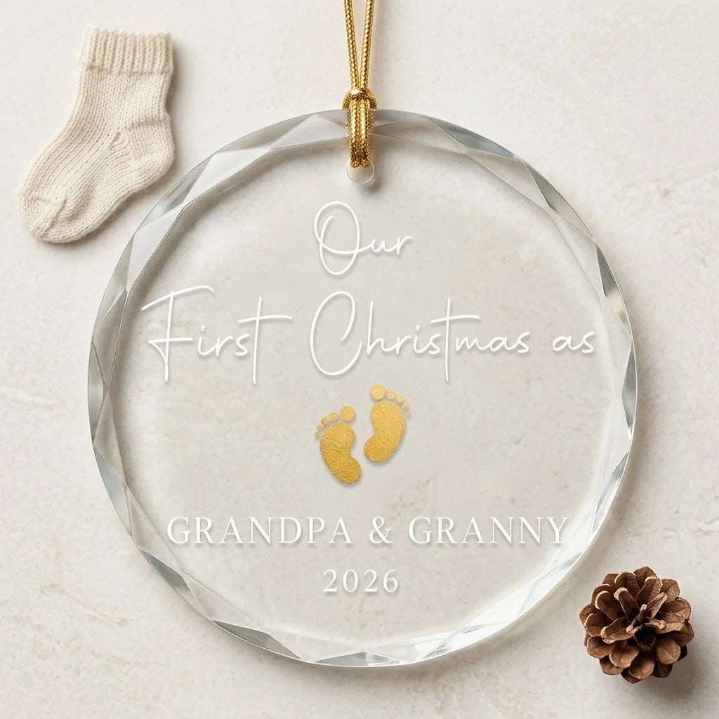Clear glass round ornament laid flat on festive wooden surface with pine branches, pinecones and holiday decorations surrounding the new grandparents design