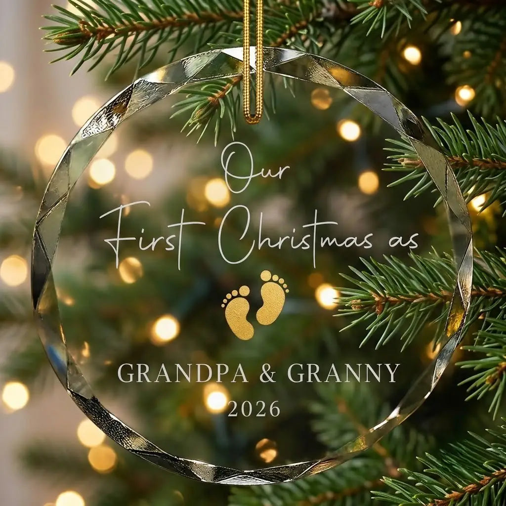 Personalized clear glass new grandparents ornament displayed hanging on Christmas tree branch with warm sparkling holiday lights background