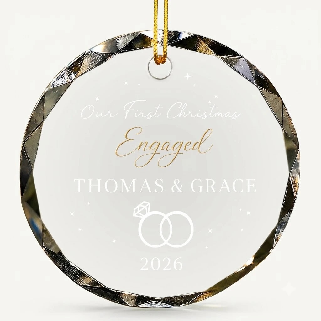 Beveled edge clear glass round ornament featuring printed interlocking wedding diamond rings graphics, custom text Our First Christmas Engaged and personalized details hanging on gold ribbon