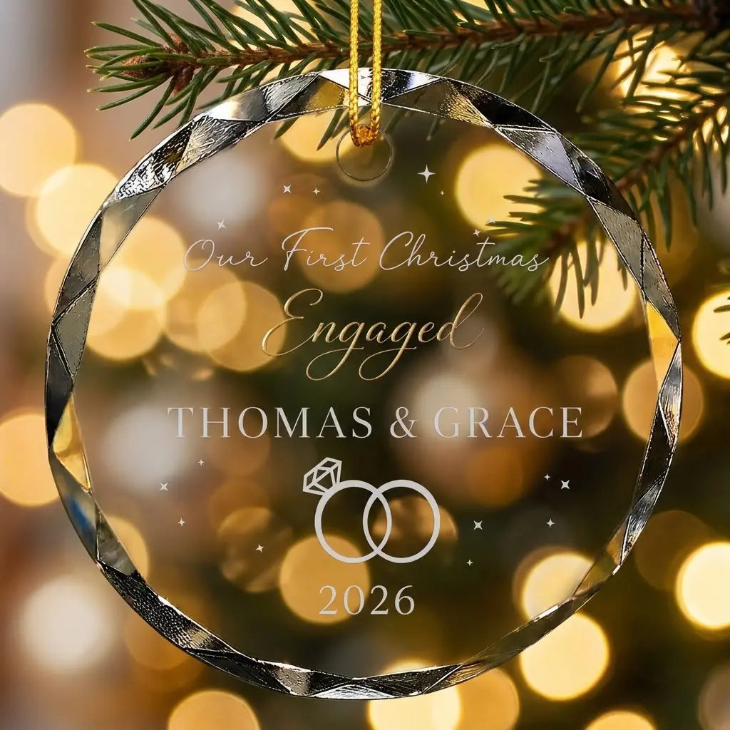 Personalized clear glass engagement ornament displayed hanging on Christmas tree branch with warm sparkling holiday lights background