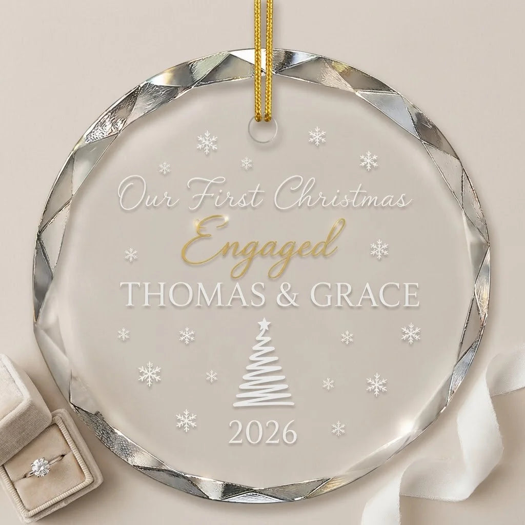 Clear glass round ornament laid flat on festive wooden surface with pine branches, pinecones and holiday decorations surrounding the engagement design