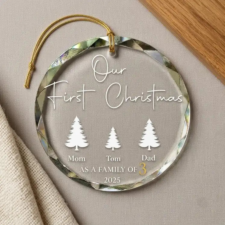 Clear glass round ornament laid flat on festive wooden surface with pine branches, pinecones and holiday decorations surrounding the family of 3 design