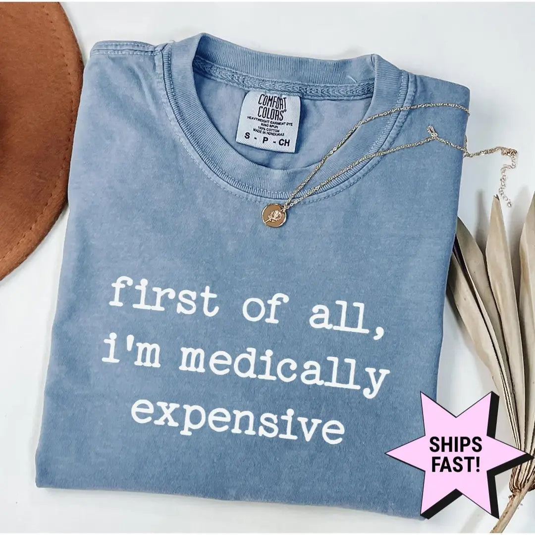 Folded Blue Jean Comfort Colors tee with first of all, i'm medically expensive in white type, a necklace on the collar