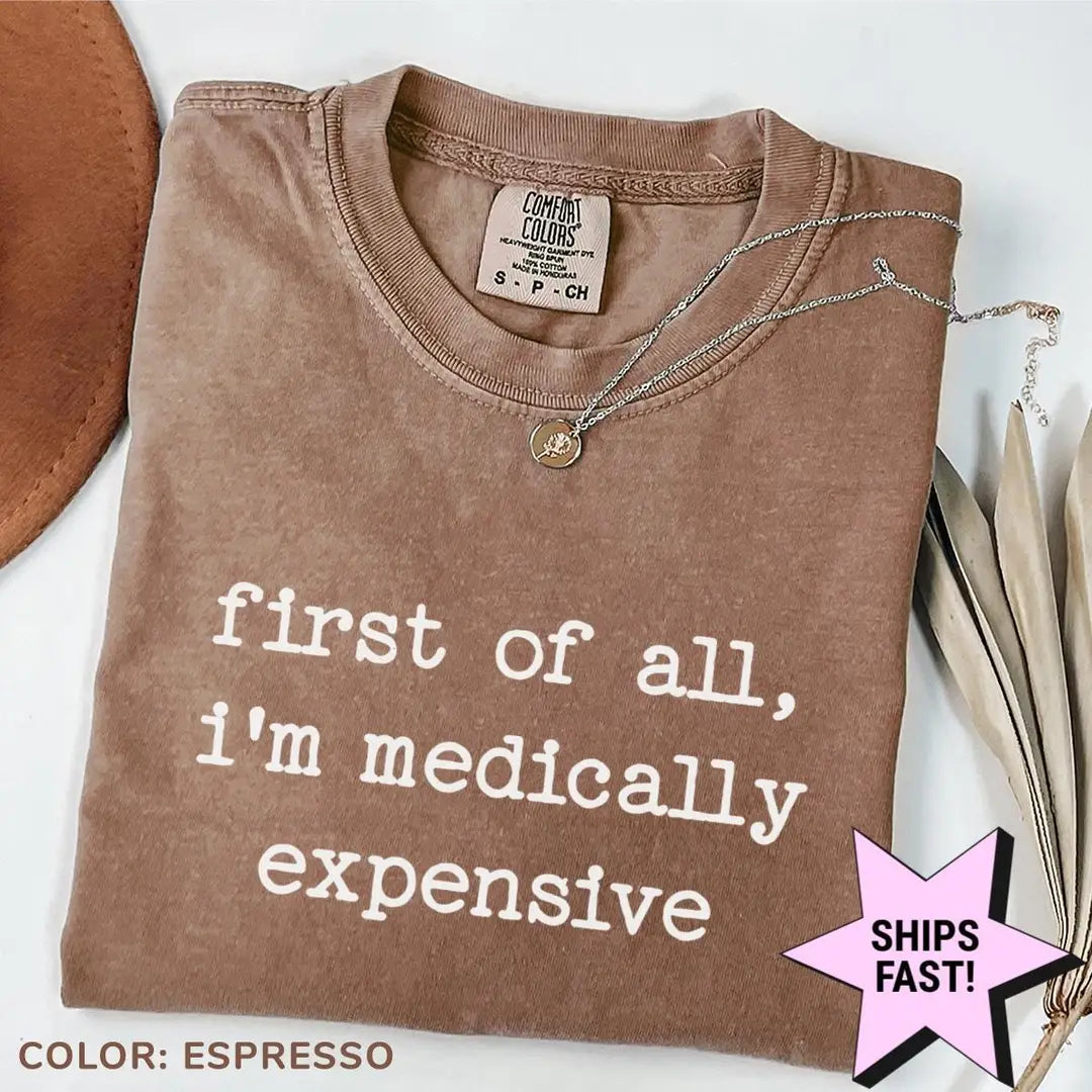 Folded Espresso brown Comfort Colors tee with first of all, i'm medically expensive across the chest, necklace on the collar