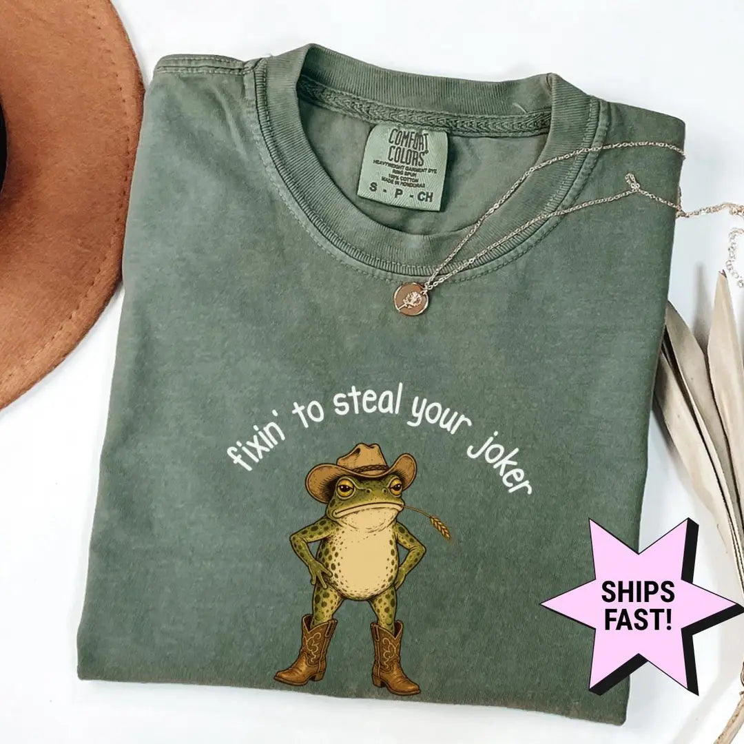 Folded Moss green Comfort Colors tee showing a cowboy frog with hands on hips and fixin' to steal your joker in white