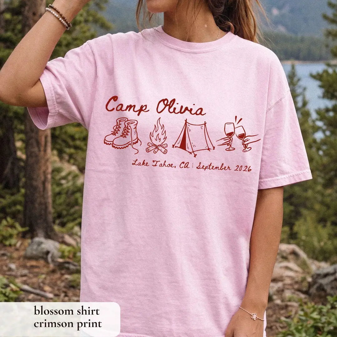 Woman in a Blossom pink Comfort Colors tee among pines, crimson Camp Olivia script with boots, campfire and tent