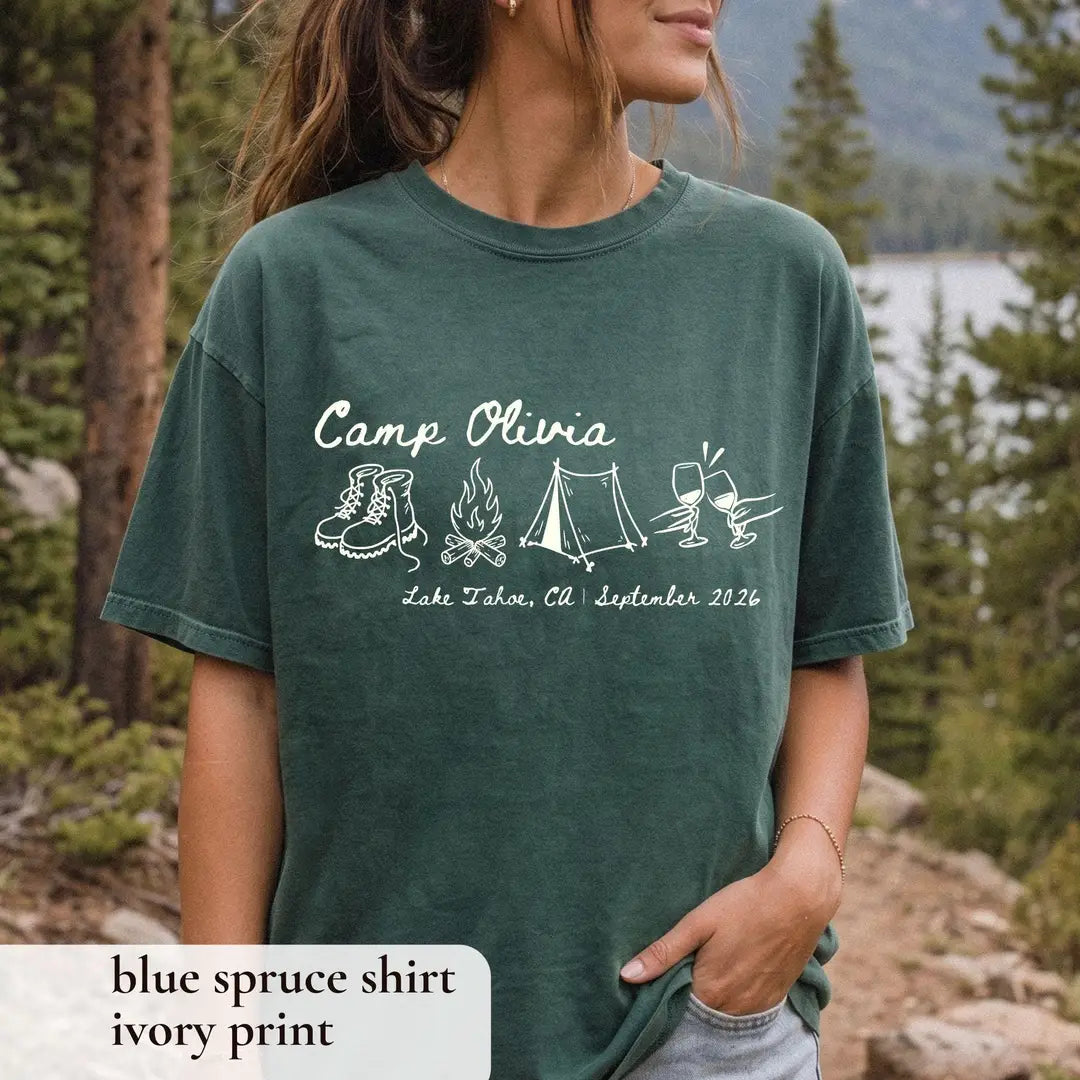 Woman in a Blue Spruce Comfort Colors tee, hand in her pocket, Camp Olivia over boots, tent and a Lake Tahoe, CA date