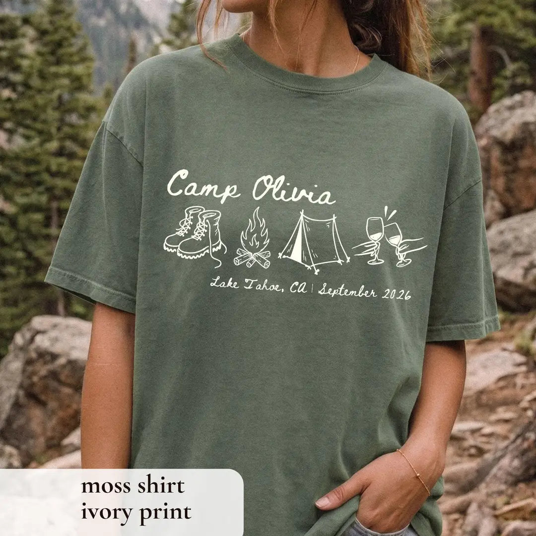 Woman in a Moss green Comfort Colors tee by a lake, ivory Camp Olivia script with boots, campfire, tent and wine