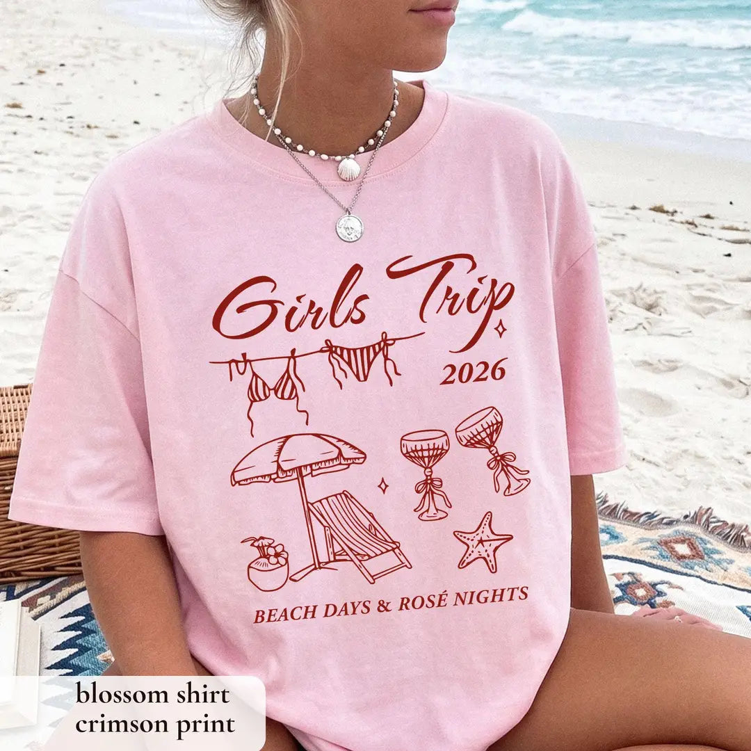 Woman in a Blossom pink Comfort Colors tee by the surf, crimson girls trip 2026 script and beach days and rose nights