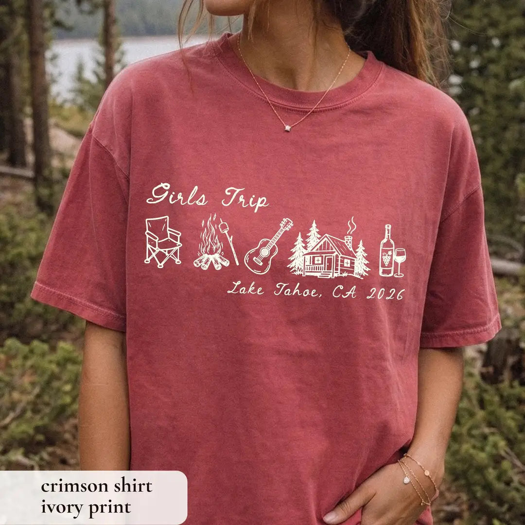Woman in a Crimson Comfort Colors tee in a pine forest, ivory girls trip script with camp chair, guitar and cabin