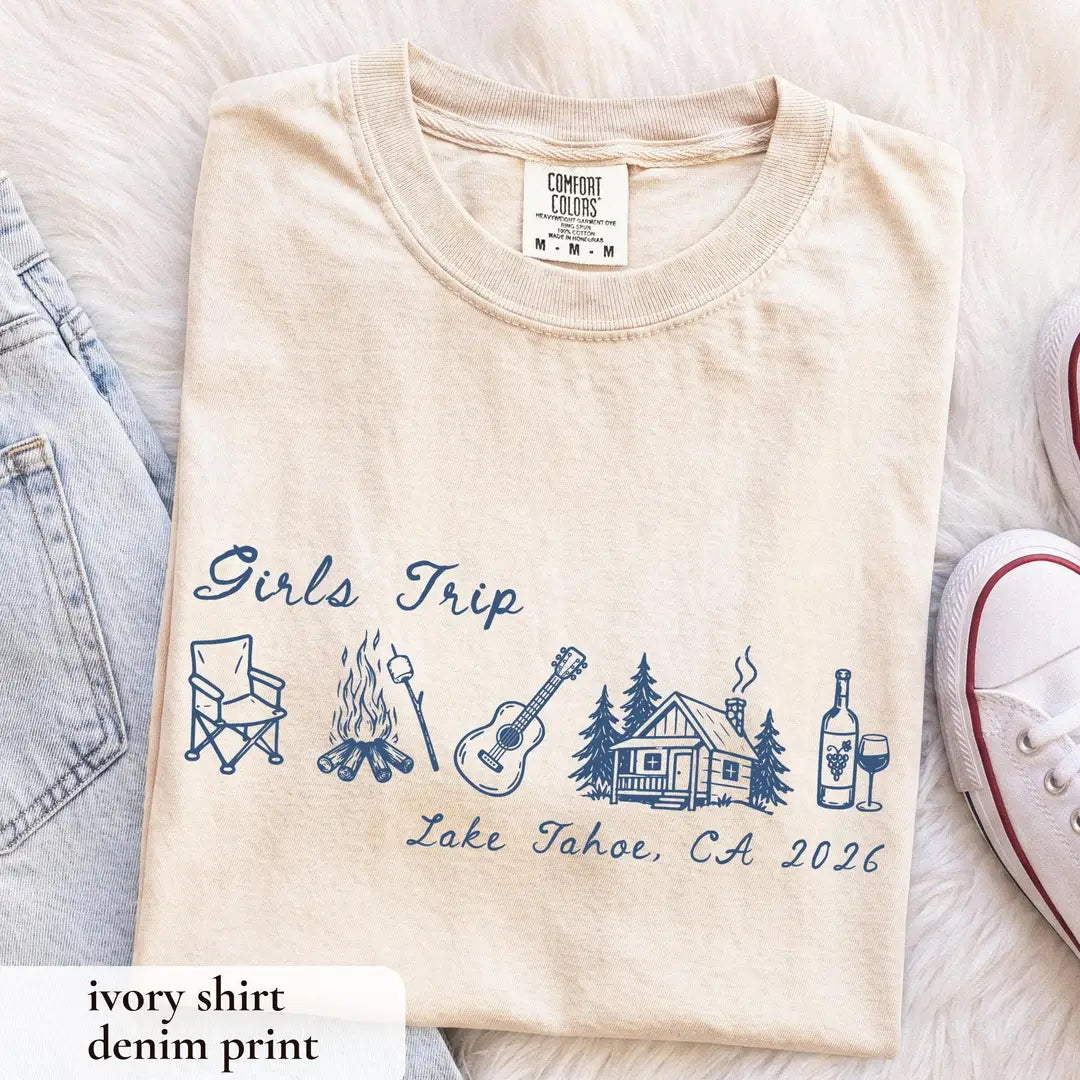 Folded Ivory Comfort Colors tee on white fur with denim blue girls trip script, camp chair, guitar and cabin