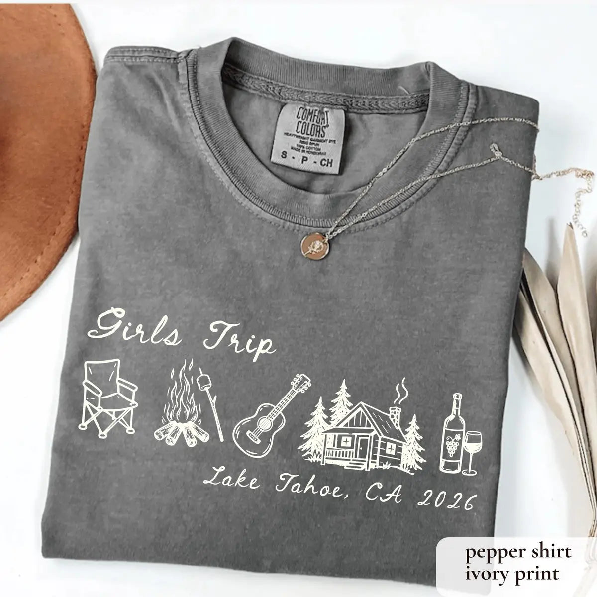 Folded Pepper Comfort Colors tee with ivory girls trip script above a camp chair, campfire, guitar, cabin and wine