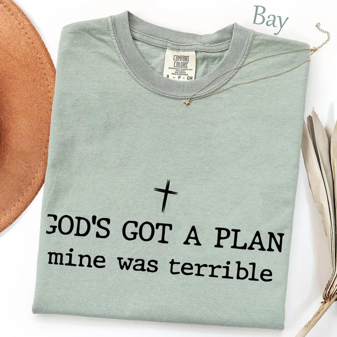 Folded Bay sage Comfort Colors tee with a small black cross above god's got a plan, mine was terrible