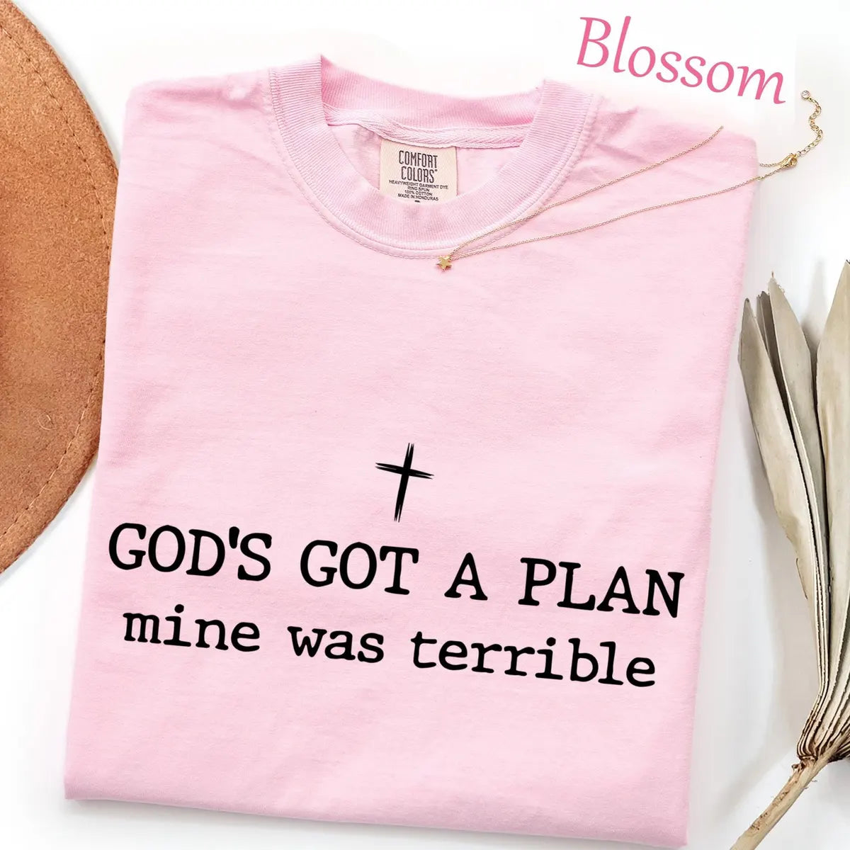 Folded Blossom pink Comfort Colors tee with a black cross above god's got a plan, mine was terrible lettering
