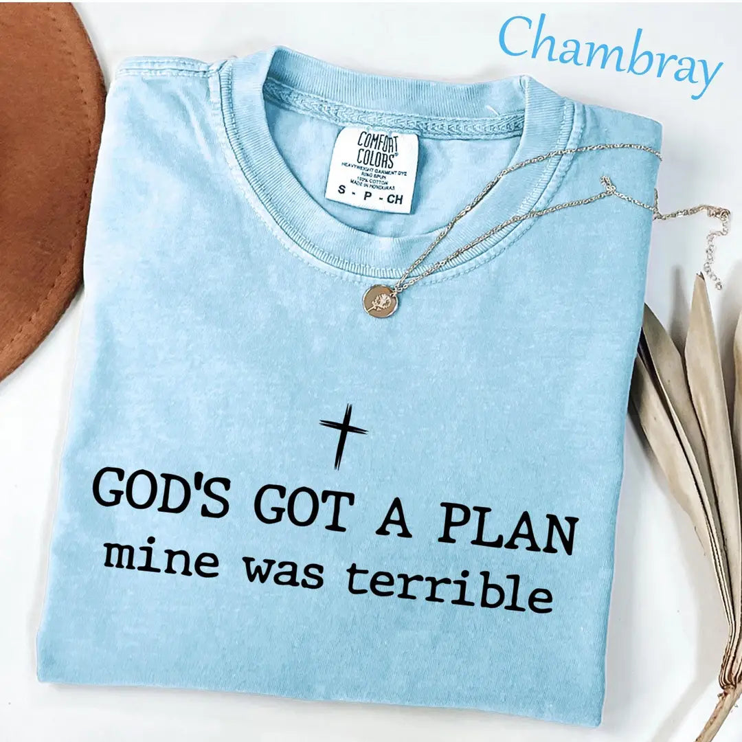 Folded Chambray blue Comfort Colors tee with a cross over black god's got a plan, mine was terrible typewriter text