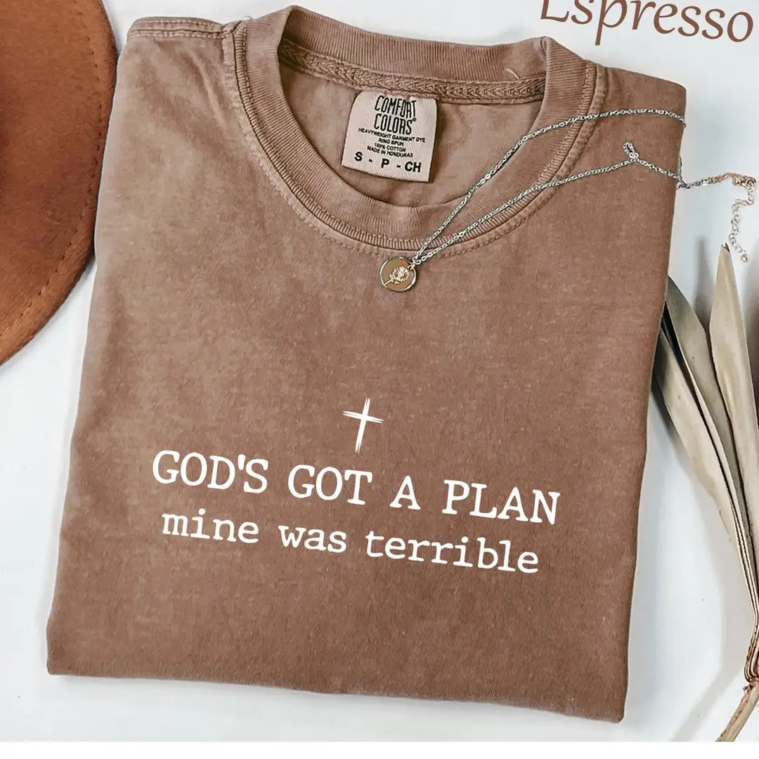 Folded Espresso brown Comfort Colors tee with a white cross and god's got a plan, mine was terrible in typewriter type
