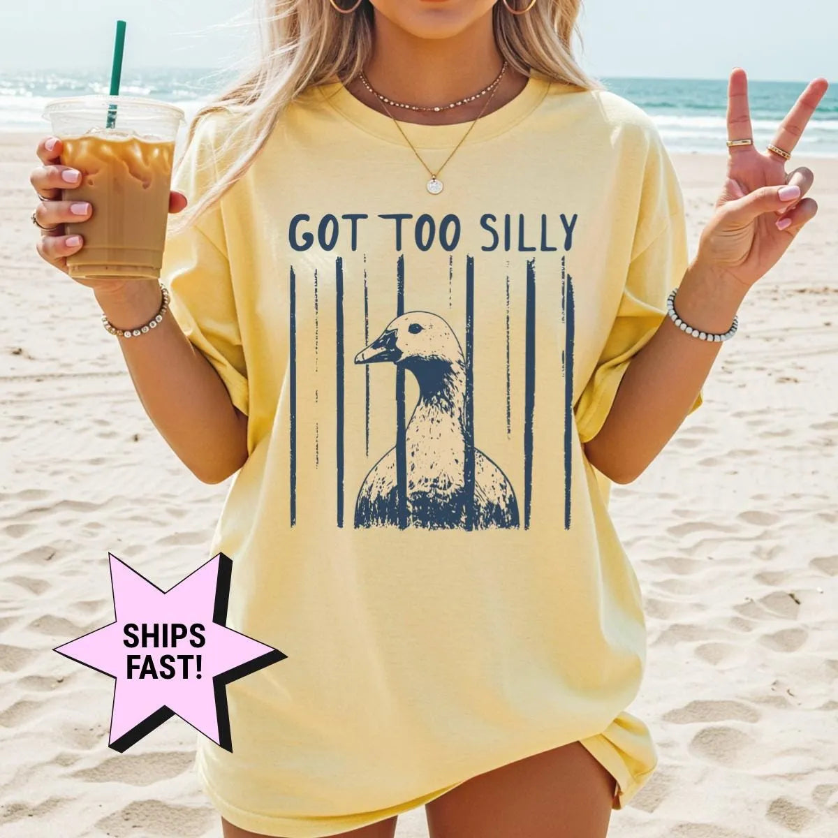 Woman in a Butter yellow Comfort Colors tee on a beach with an iced coffee, got too silly and a navy goose head print