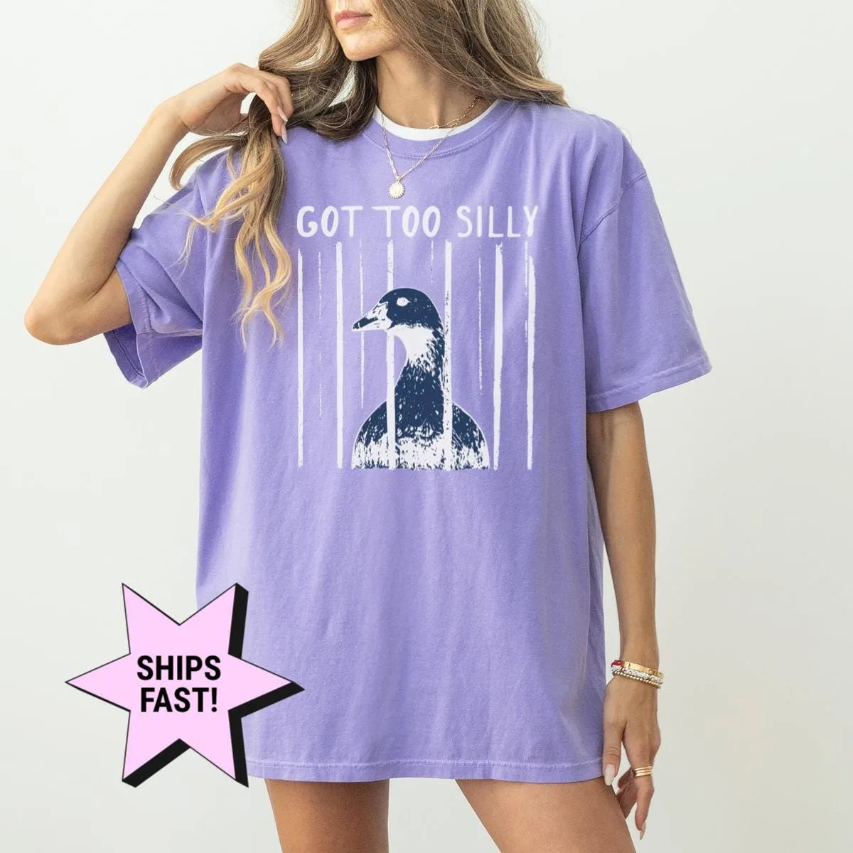 Woman in a Violet Comfort Colors tee, hand at her hair, with got too silly over a goose head and vertical white stripes