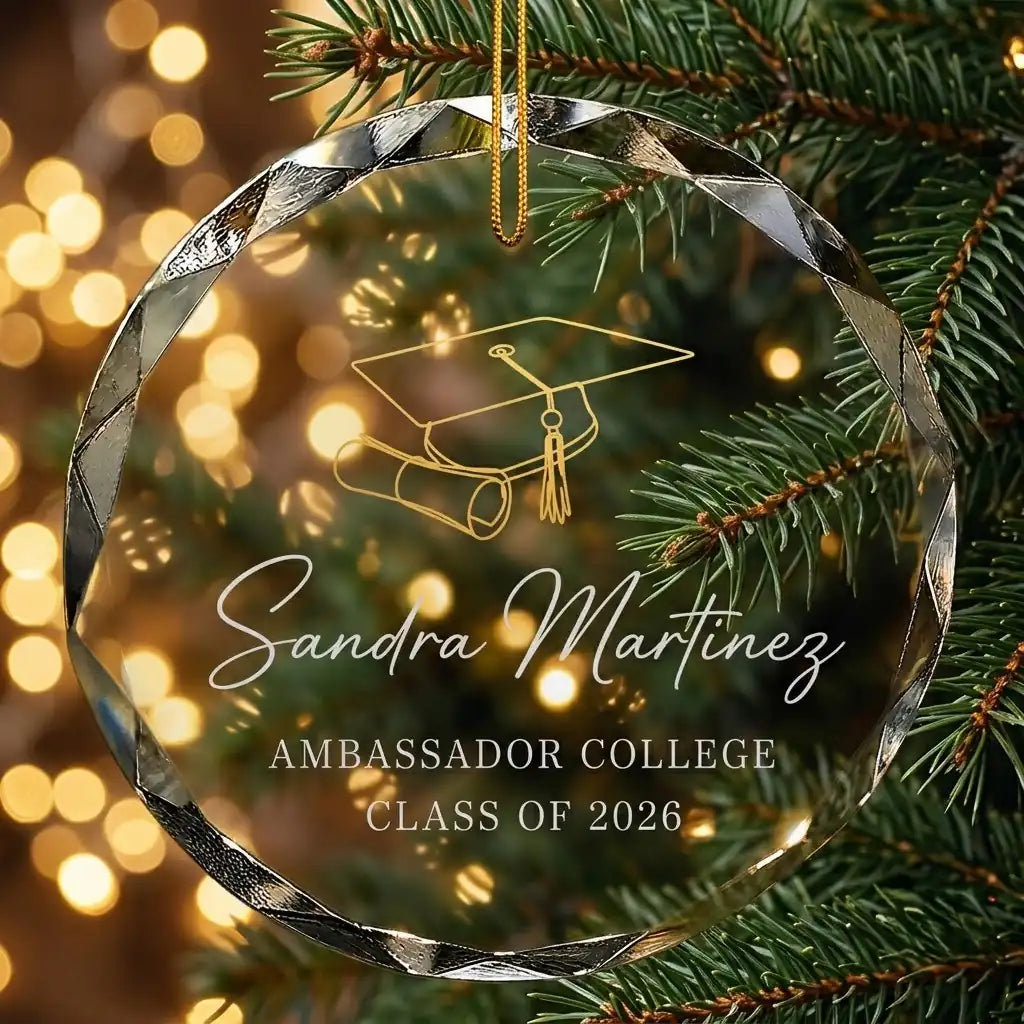 Personalized clear glass graduation ornament displayed hanging on Christmas tree branch with warm sparkling holiday lights background