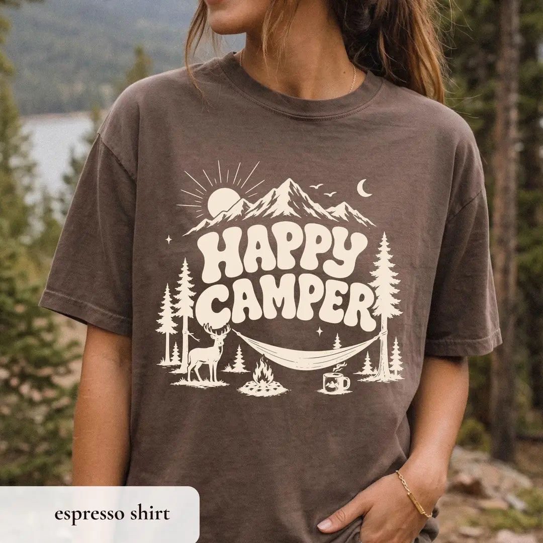 Woman in an Espresso brown Comfort Colors tee in a pine forest, ivory happy camper, mountain, deer and coffee mug