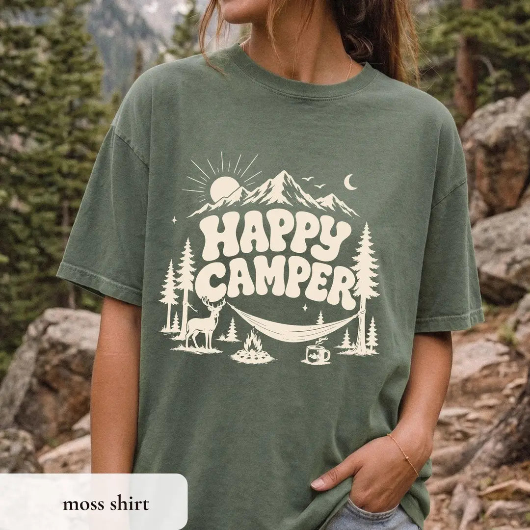 Close view of a Moss green Comfort Colors tee with ivory happy camper lettering, sun and moon, hammock and campfire