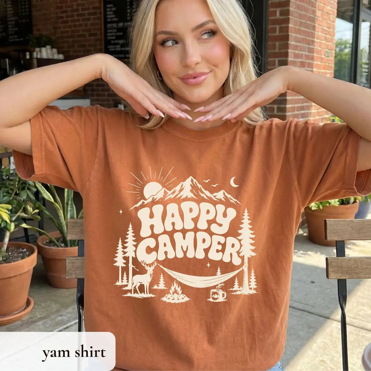 Woman in a Yam orange Comfort Colors tee outside a cafe, hands under her chin, ivory happy camper and mountain design