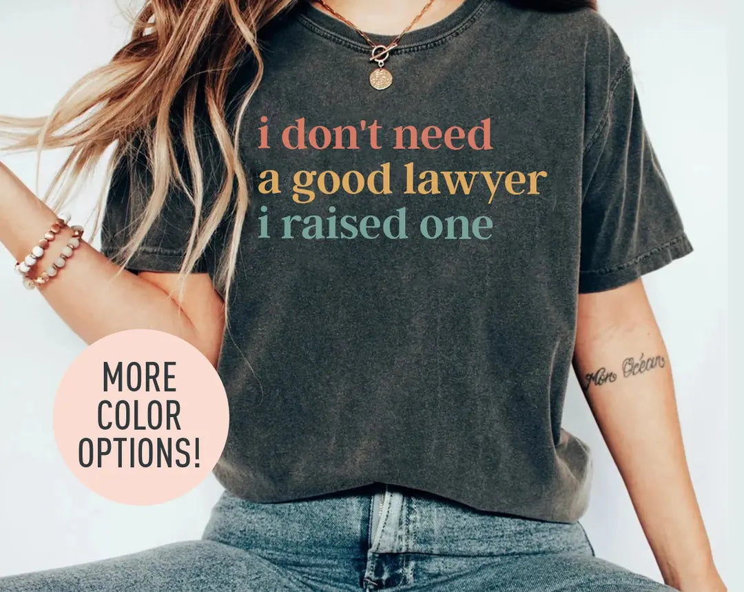 Woman in a dark gray Comfort Colors tee and jeans, bracelets on her wrist, with a three-line good lawyer i raised one quote
