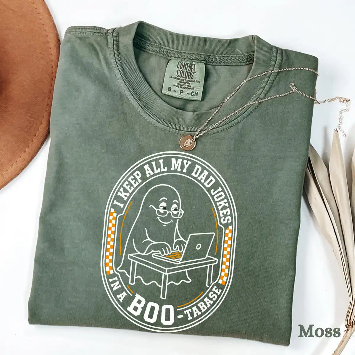 Comfort Colors T-shirt flatlay in Moss color featuring I Keep All My Dad Jokes In A Bootabase ghost graphic