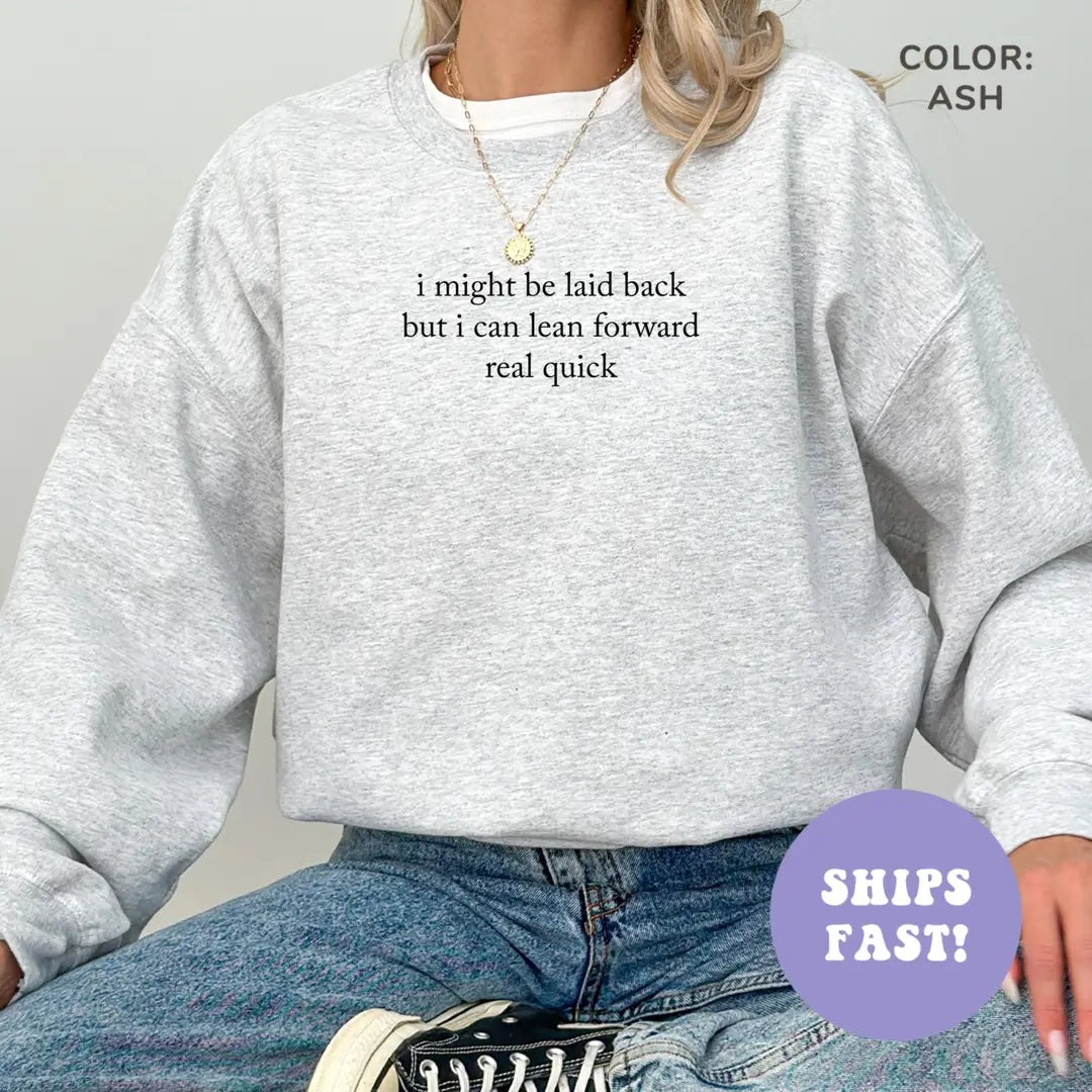 Woman in an Ash crewneck sweatshirt and jeans, small black serif quote, I might be laid back but I can lean forward