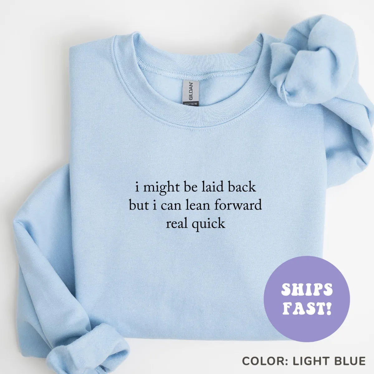 Light Blue crewneck sweatshirt laid flat with a rolled sleeve, dark serif quote I might be laid back but I can lean forward