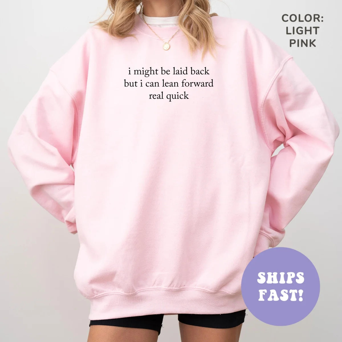 Woman in an oversized Light Pink sweatshirt, hands in pockets, small dark quote, I might be laid back but I can lean forward