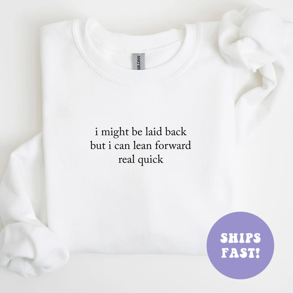 White sweatshirt laid flat with a bunched sleeve, black serif quote, I might be laid back but I can lean forward real quick