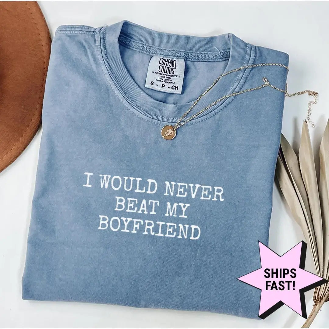 Folded Blue Jean Comfort Colors tee with I WOULD NEVER BEAT MY BOYFRIEND stacked in white capitals, necklace above