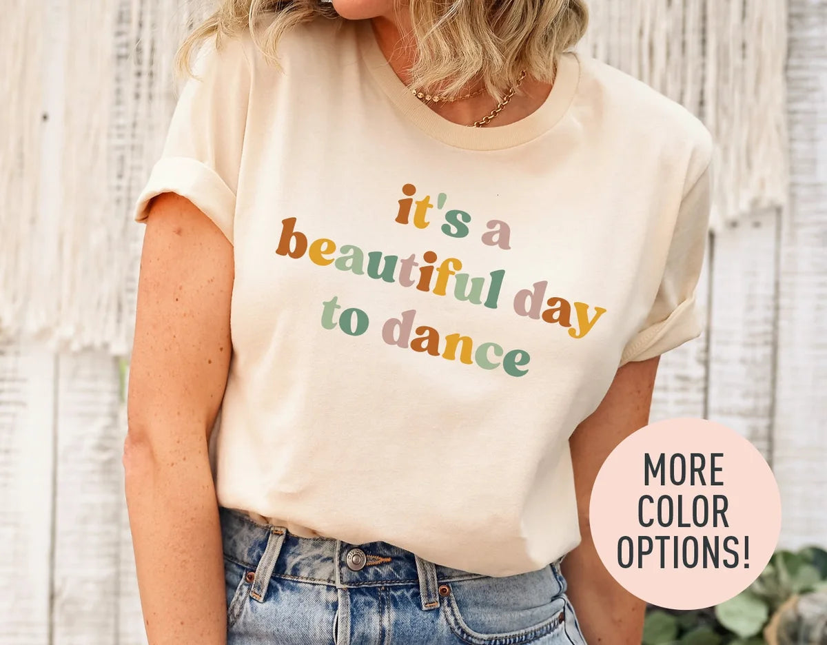 Woman in a natural cream tee with rolled sleeves and jeans, it's a beautiful day to dance in rust, sage and rose lettering