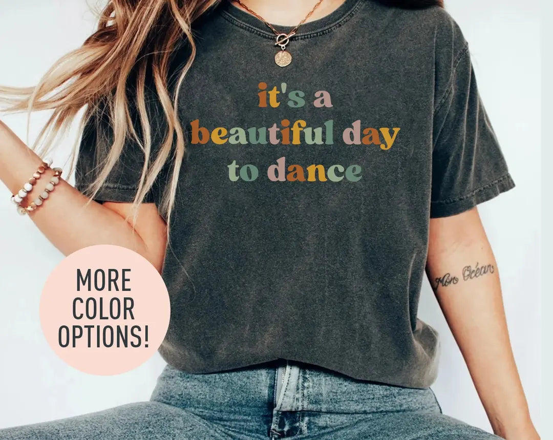 Woman in a dark gray Comfort Colors tee and jeans, bracelets on her wrist, with it's a beautiful day to dance in retro type