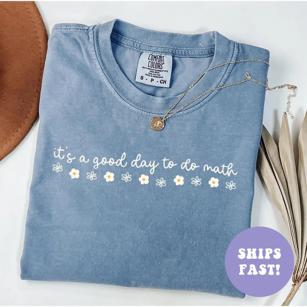 Folded Blue Jean Comfort Colors tee with the cursive do math quote and a row of white daisies, necklace on the collar