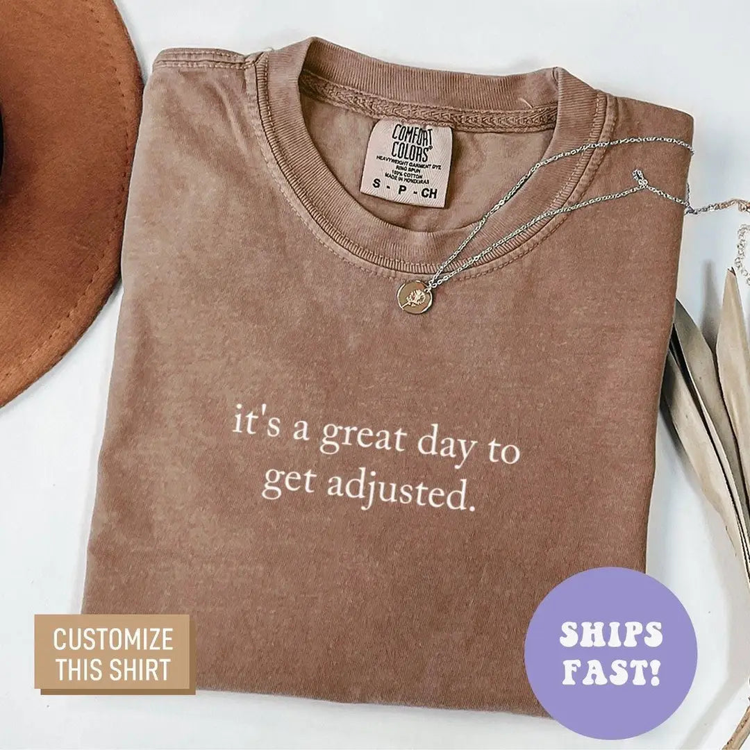 Folded Espresso brown Comfort Colors tee with the get adjusted quote in light serif letters, necklace on the collar